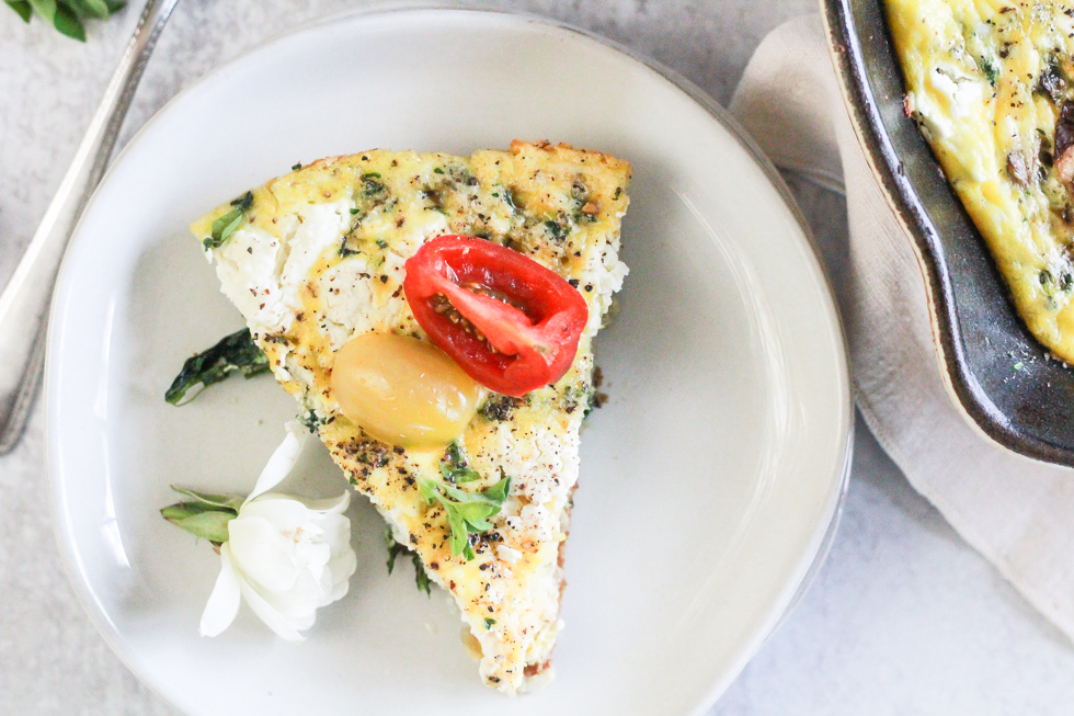 Horizontal image of a slice of vegetarian frittata on a white plate with a white rose garnish.