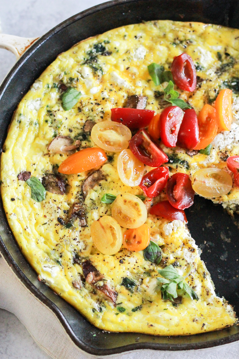 Closeup of a vegetarian frittata in a skillet with one slice missing.