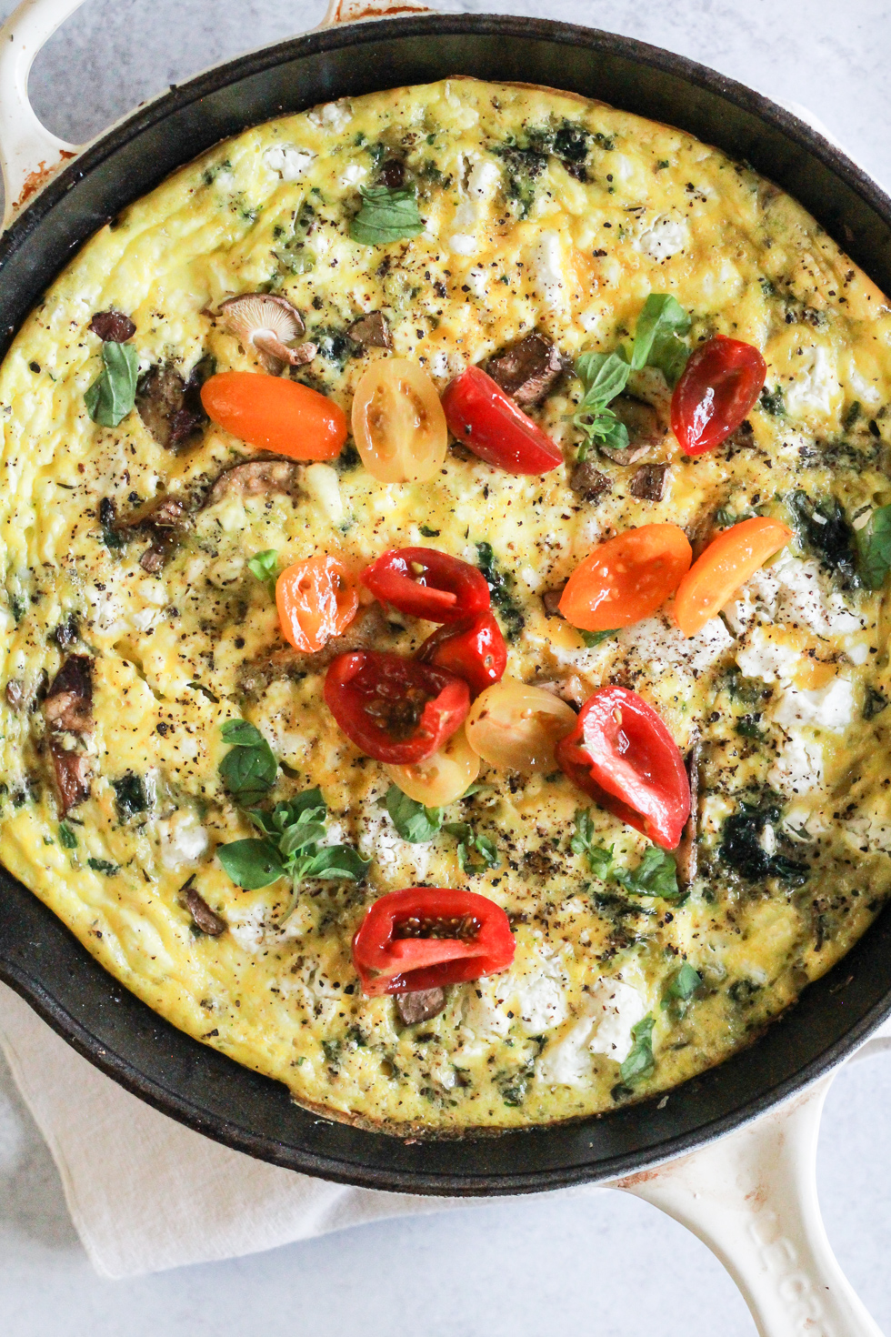Vegetarian Frittata topped with cherry tomatoes in a white skillet.