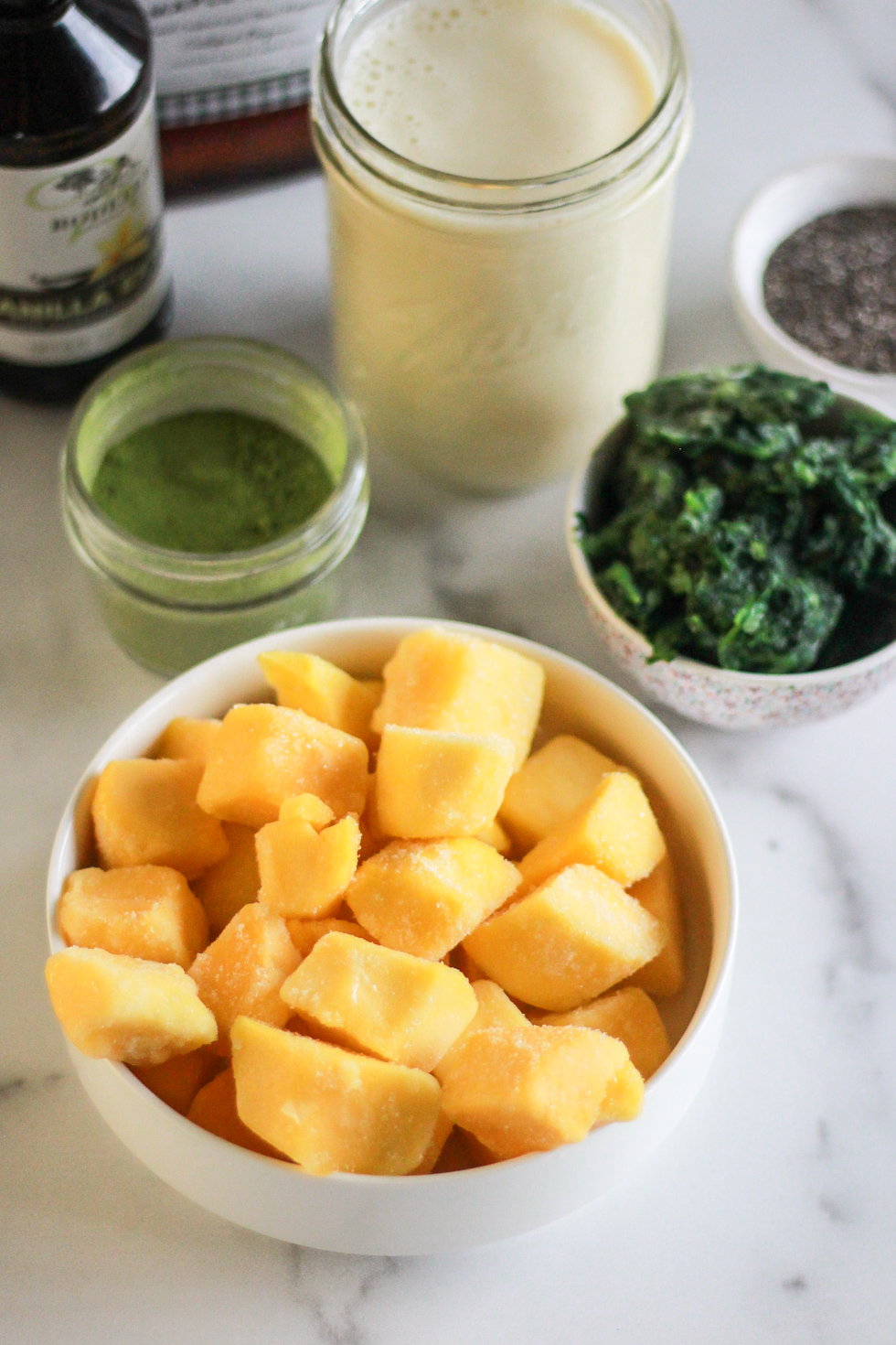 Bowls of mango, spinach, matcha, and chia seeds to make a green smoothie.