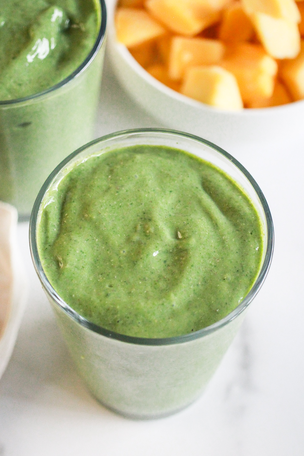 Green smoothies next to a bowl of frozen mangoes