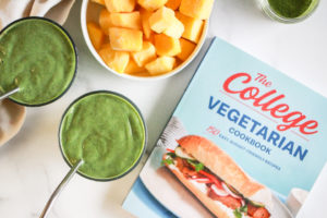 The College Vegetarian Cookbook with green smoothies and a bowl of frozen mango.