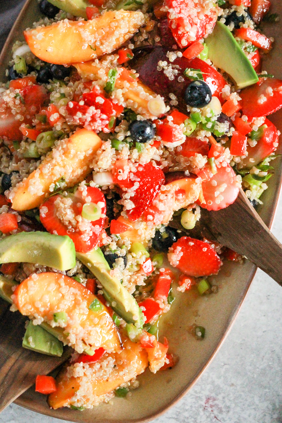 Wooden spoons mixing summer quinoa salad with fruit.