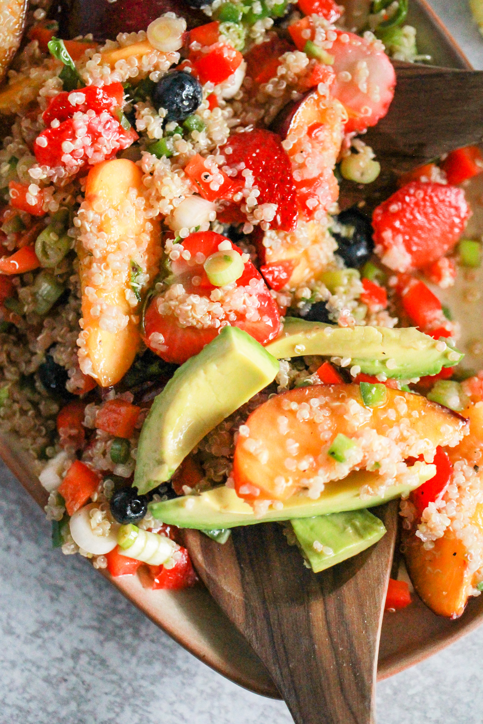 Quinoa salad with avocado and fruit on tan platter with wood spoons.