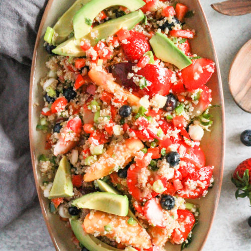 Summer Quinoa Salad on tan platter with wooden serving spoons.