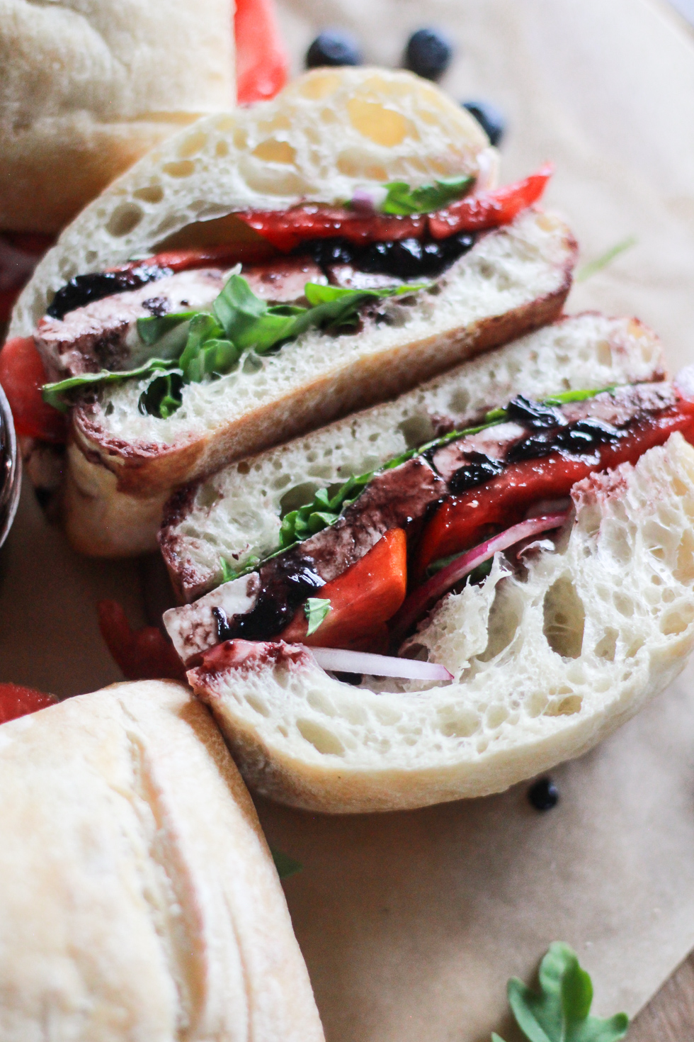 Halved Tomato Mozzarella Sandwich with arugula and blueberry balsamic sauce.