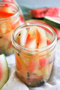 Watermelon rind pickles in glass mason jars with sliced watermelon in background