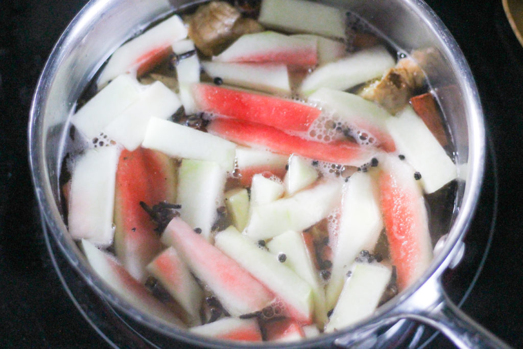 Watermelon rind pieces in steel pot on black stovetop.