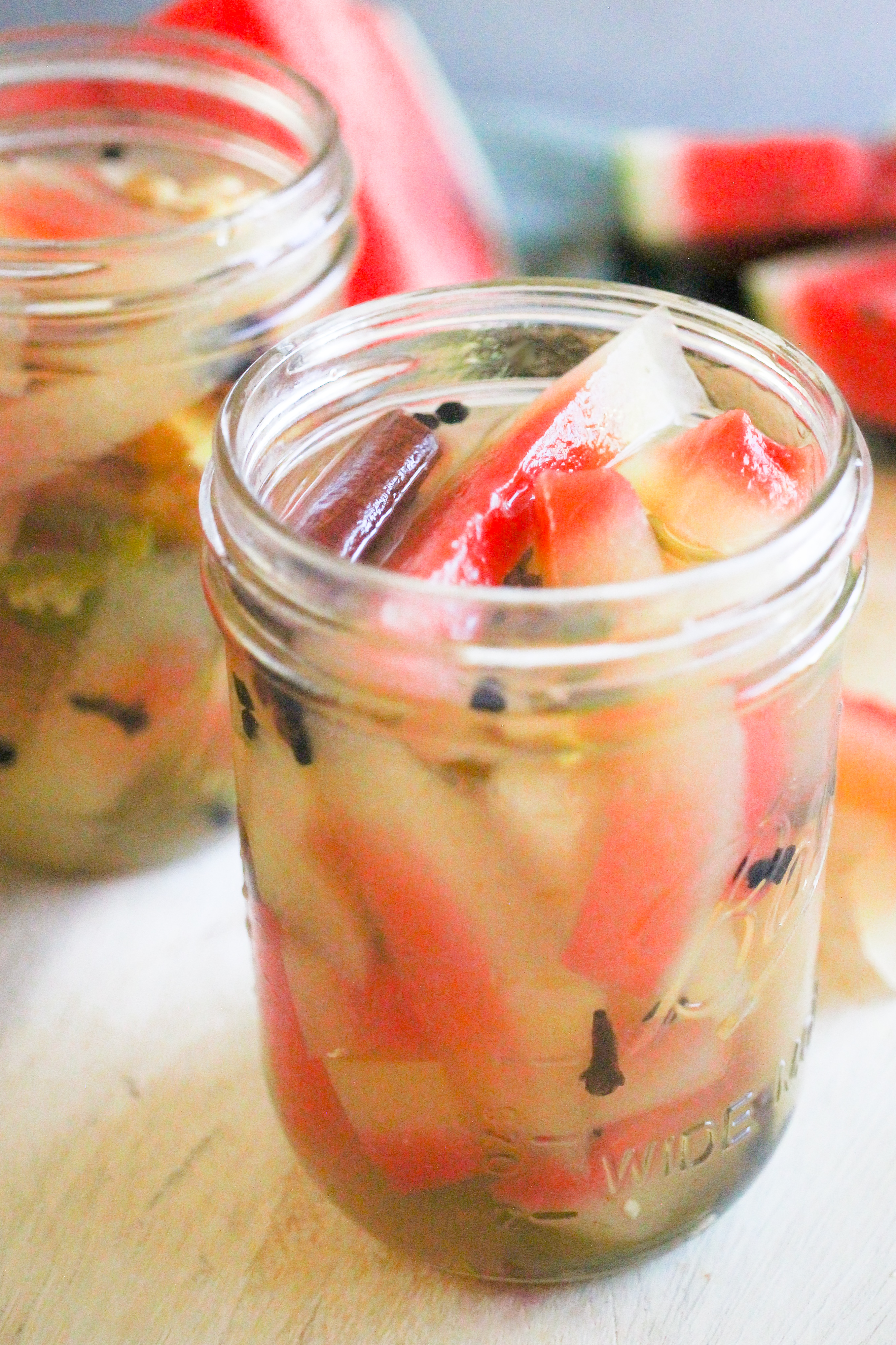 Pickled watermelon rind in two glass mason jars with sliced watermelon in the background