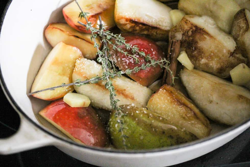 Apples, pears, cinnamon, and fresh thyme in a white Dutch oven.