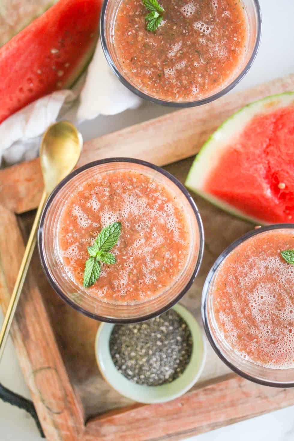 Overhead image of Watermelon Chia Fresca in glasses on a wood tray with a gold spoon.