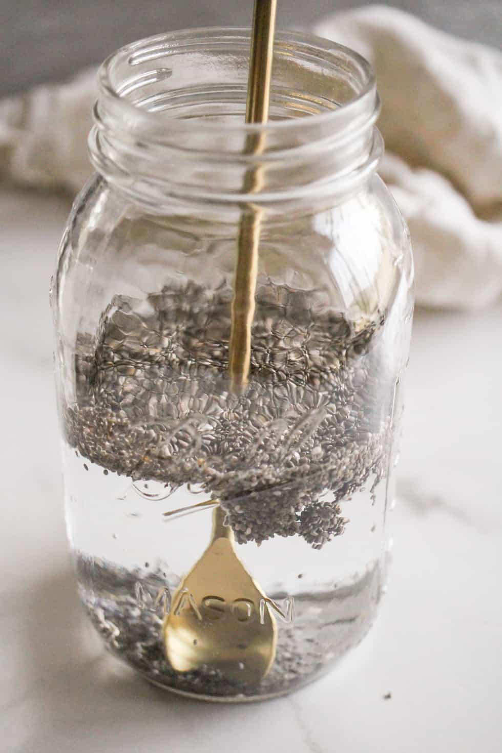 Chia seeds in a jar of water being stirred with a gold spoon.