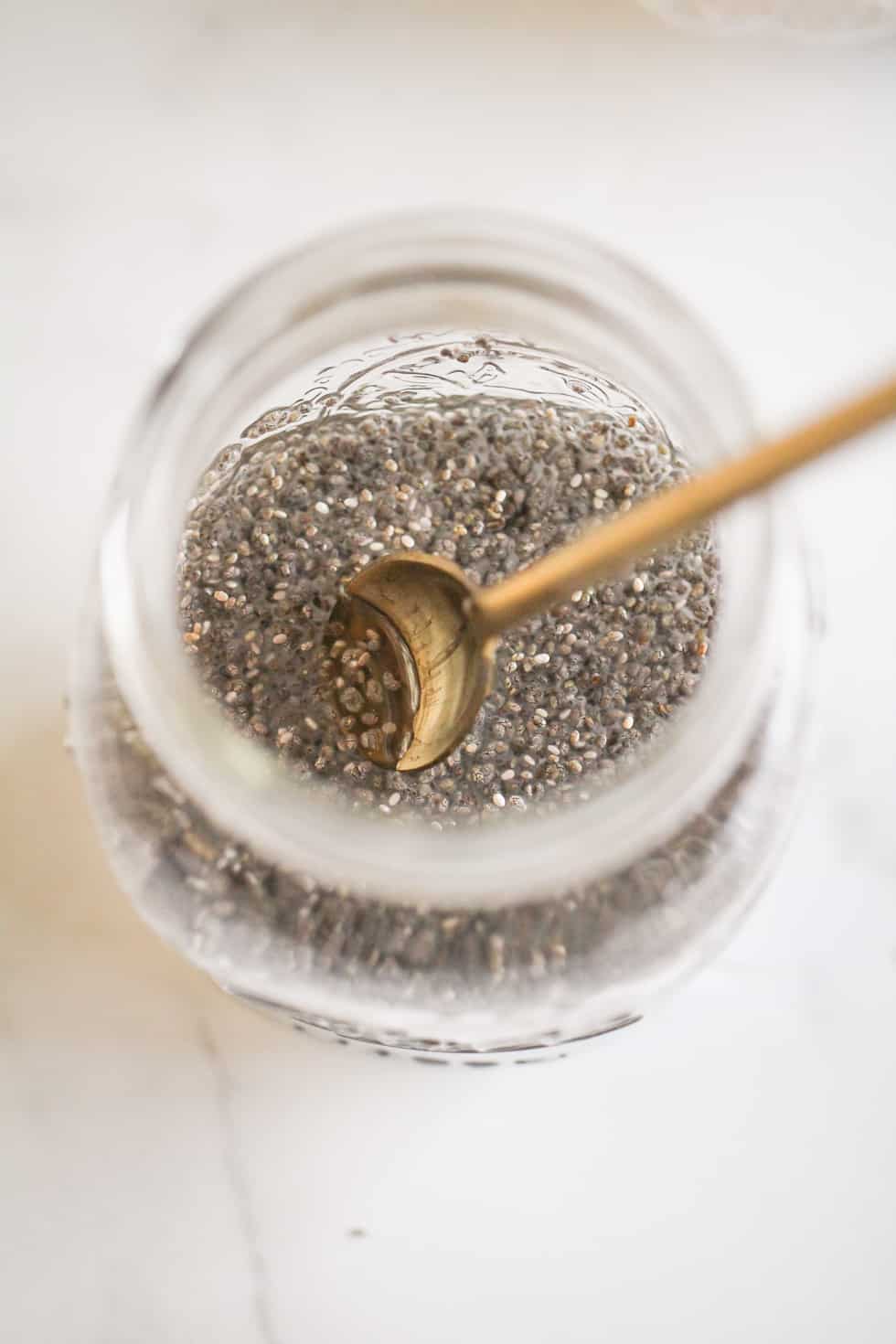 Chia gel or chia water in a glass jar with gold stirring spoon.