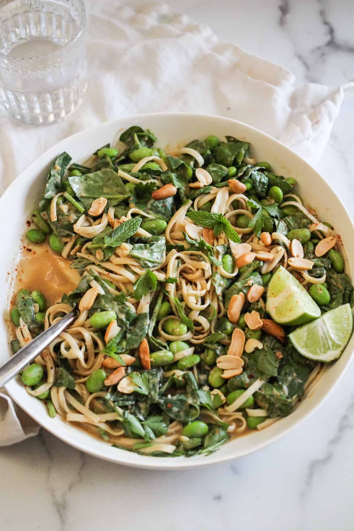 Peanut noodles with edamame and lime in a white bowl on a marble counter. 