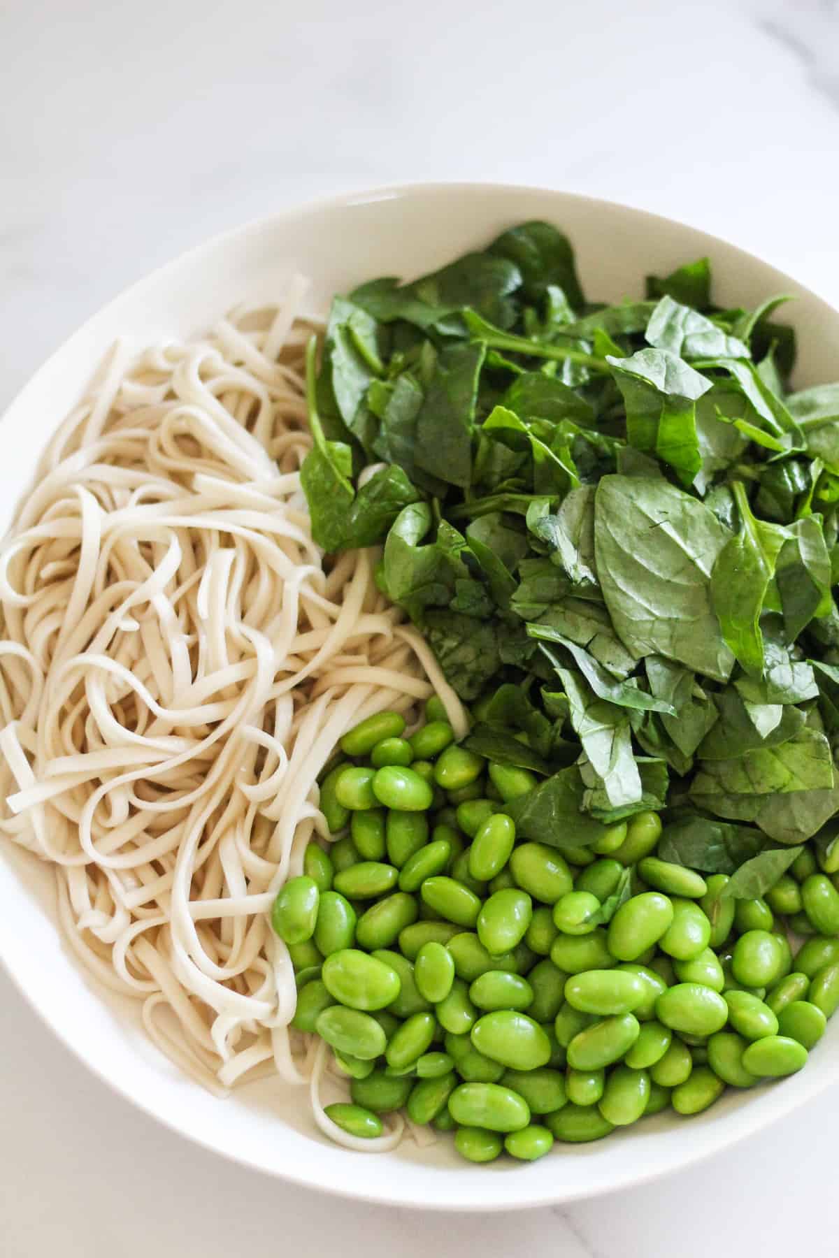Noodles, edamame, and chopped spinach in a white bowl.