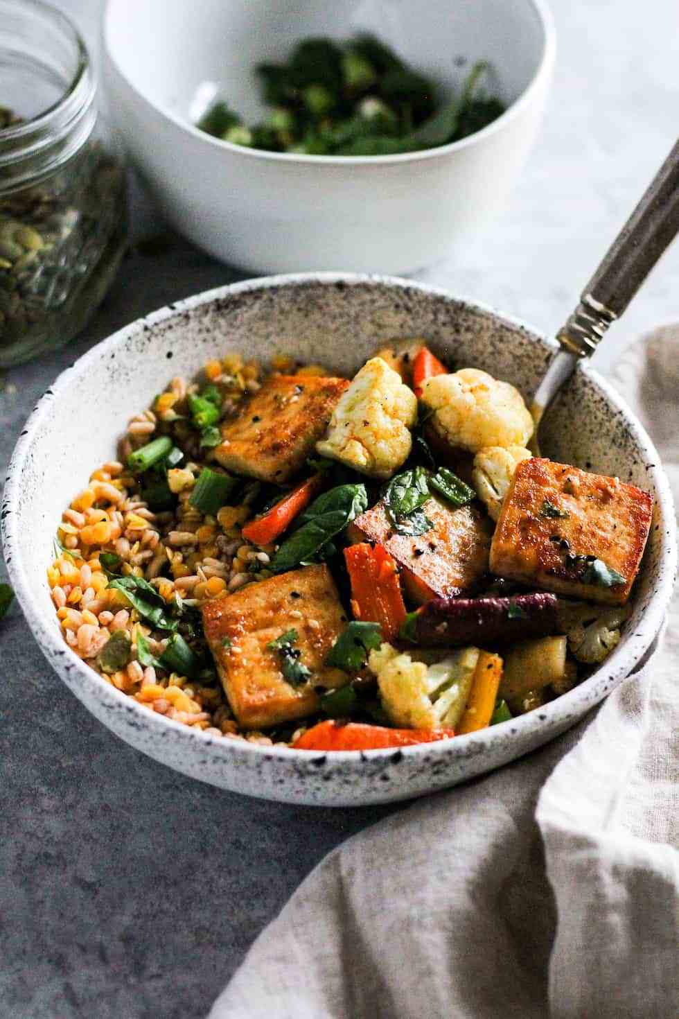 Tofu and veggies in white bowls on grey background.