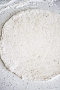 Pizza dough with herbs and garlic rolled out on floured countertop.
