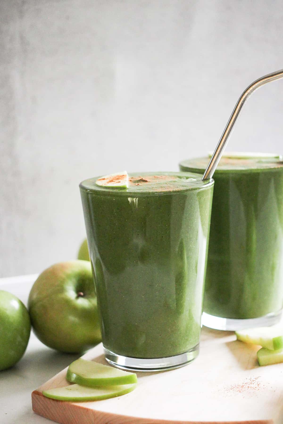 Two green lentil smoothies in glasses with green apples behind them.