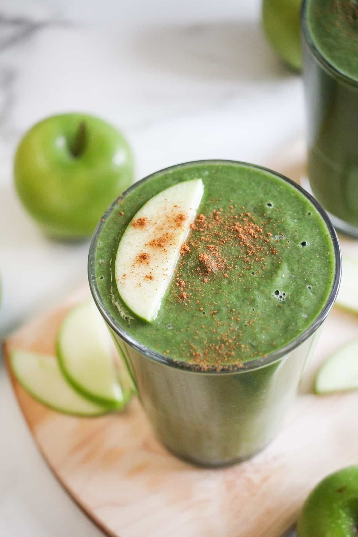 Green apple lentil smoothie in a glass garnished with apple slice and cinnamon.