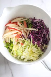 Sliced apples, cabbage, celery, and green onion in a large mixing bowl.