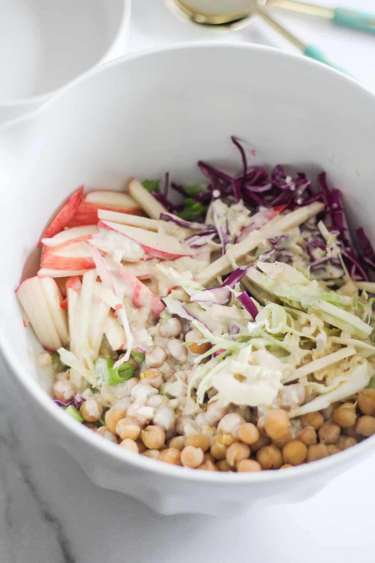 Cabbage, chickpeas, and apples with creamy dressing in a large white mixing bowl.