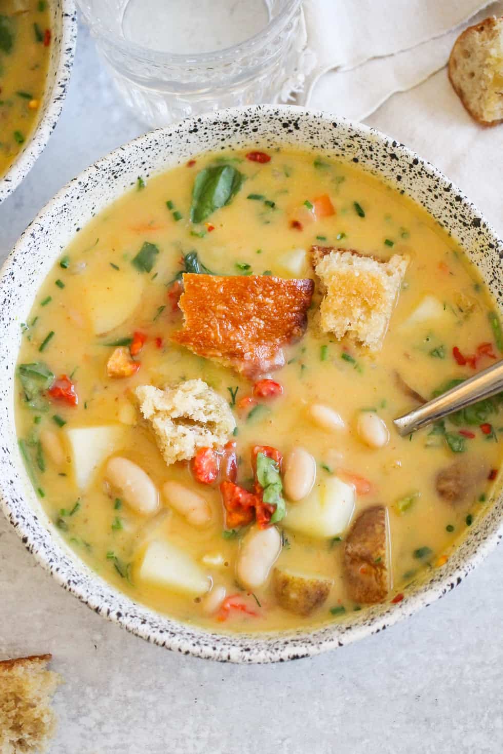 Vegan potato soup in white ceramic bowl against gray background.