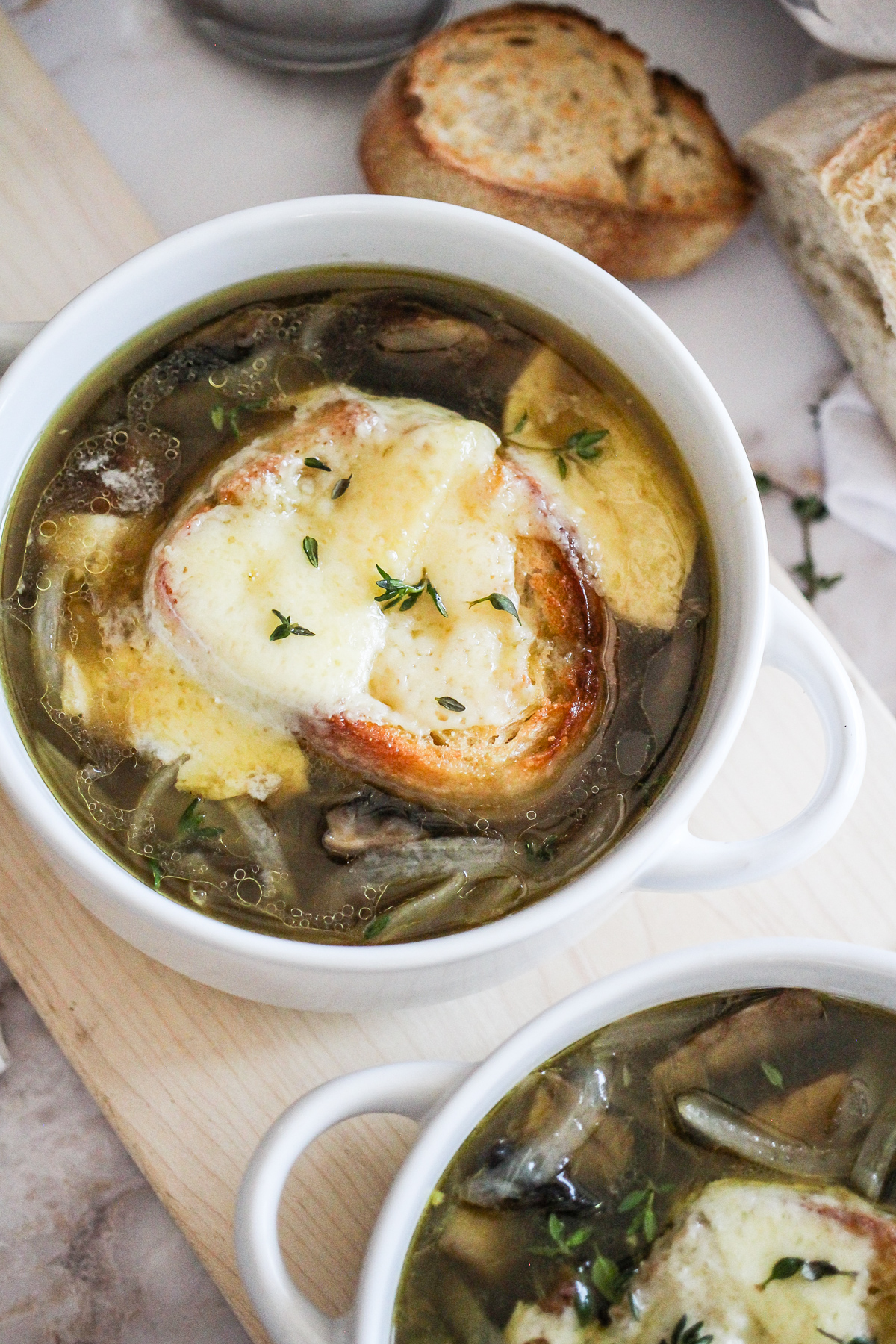 Closeup of French Onion Soup in a white crock with loaf of bread behind it.