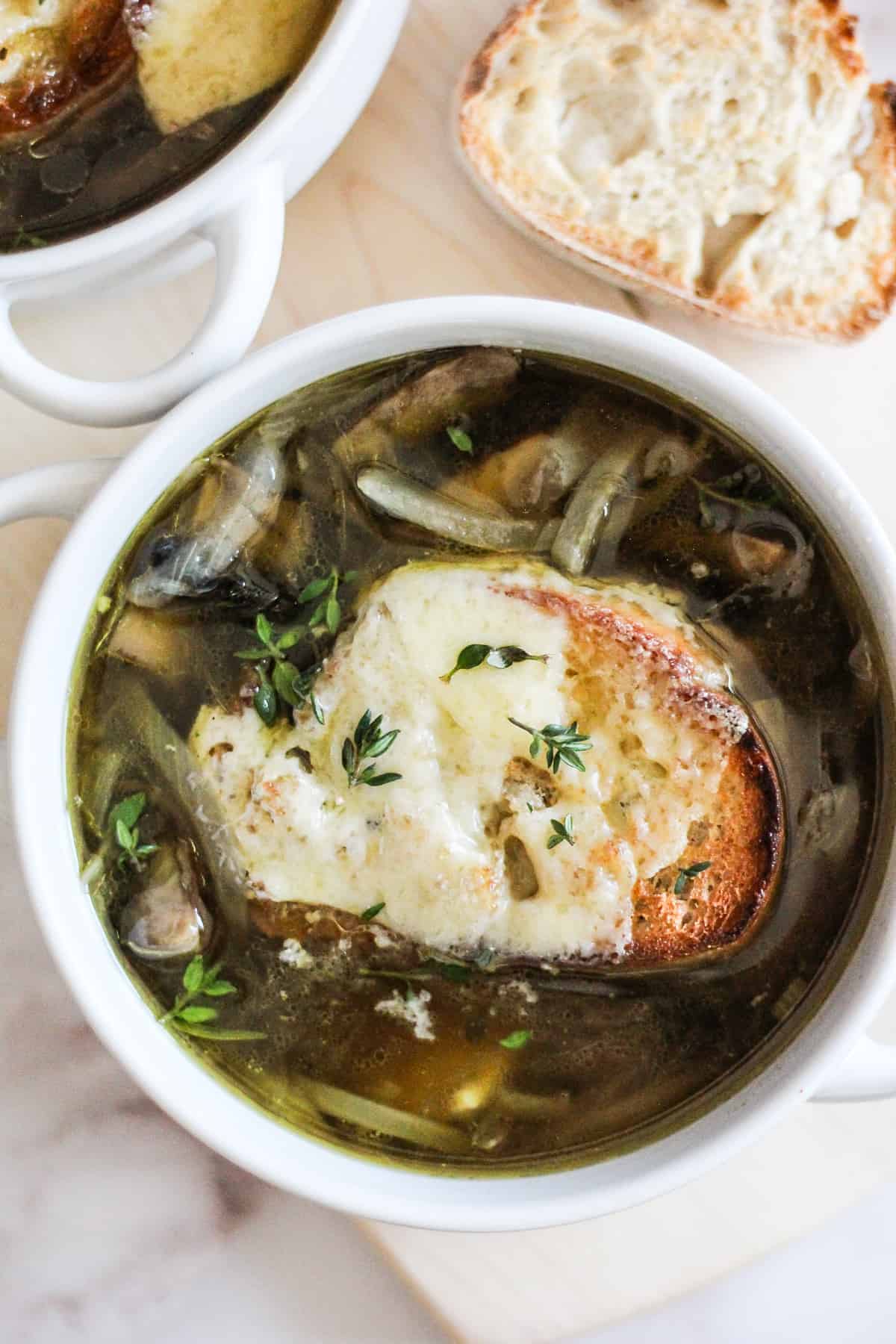 Vegetarian French Onion Soup with portobello mushrooms in a white soup crock on a wood board.