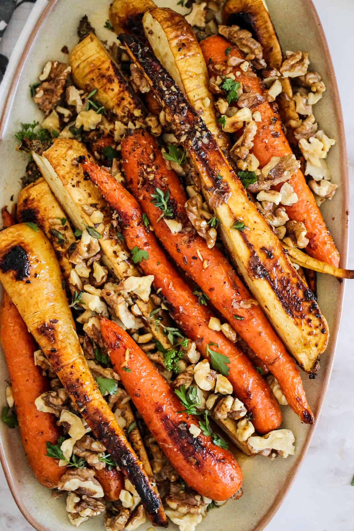 Honey roasted carrots and parsnips on beige serving platter with walnuts and fresh herbs.