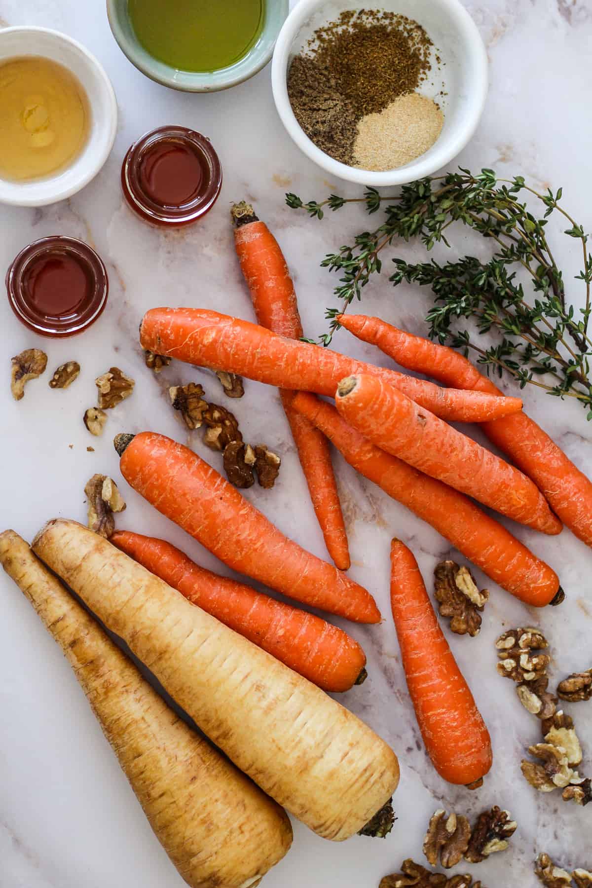 Parsnips, carrots, honey, walnuts, fresh thyme, and dry spices on white marble.