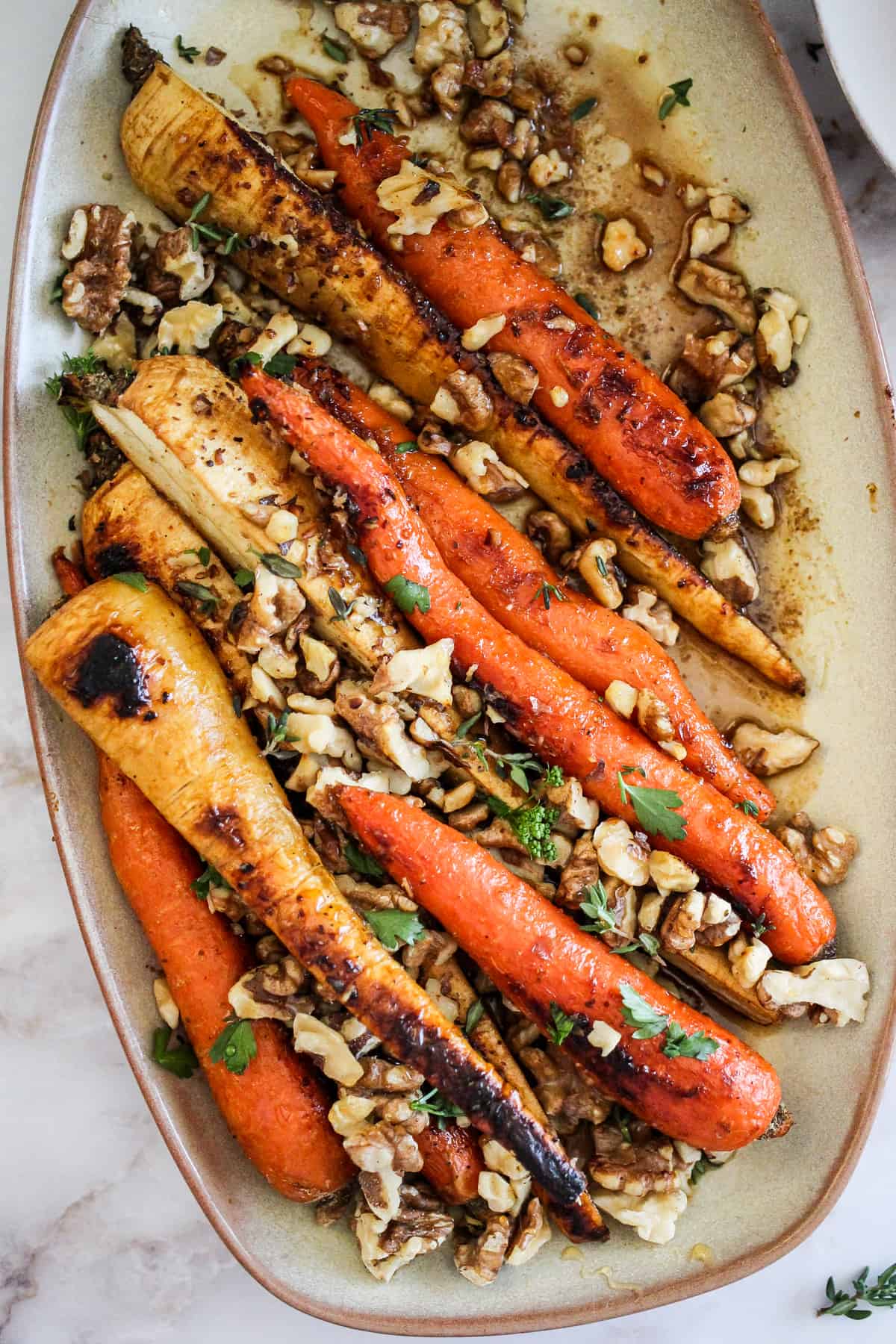 Overhead image of roasted carrots and parsnips on a beige serving platter.