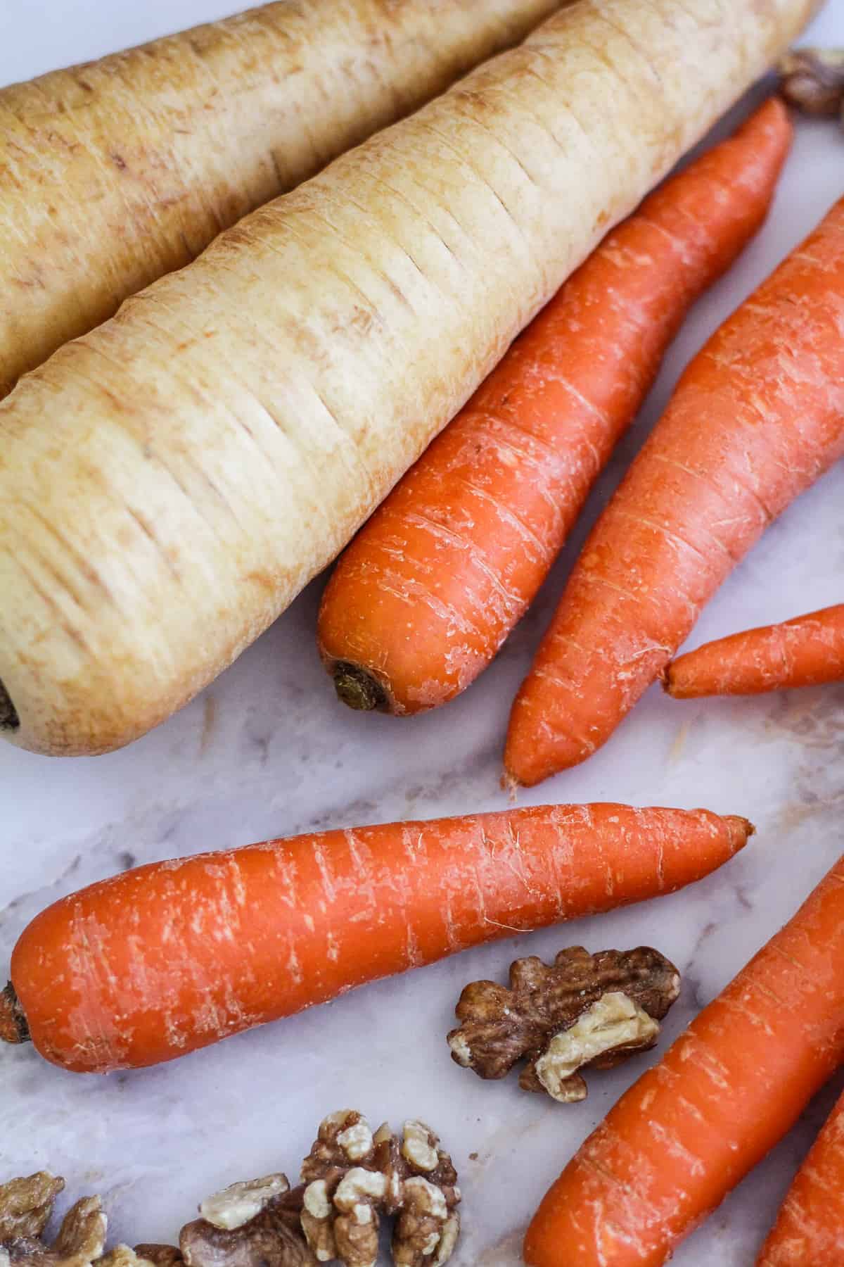 Whole parsnips, whole carrots, and walnuts on white marble.