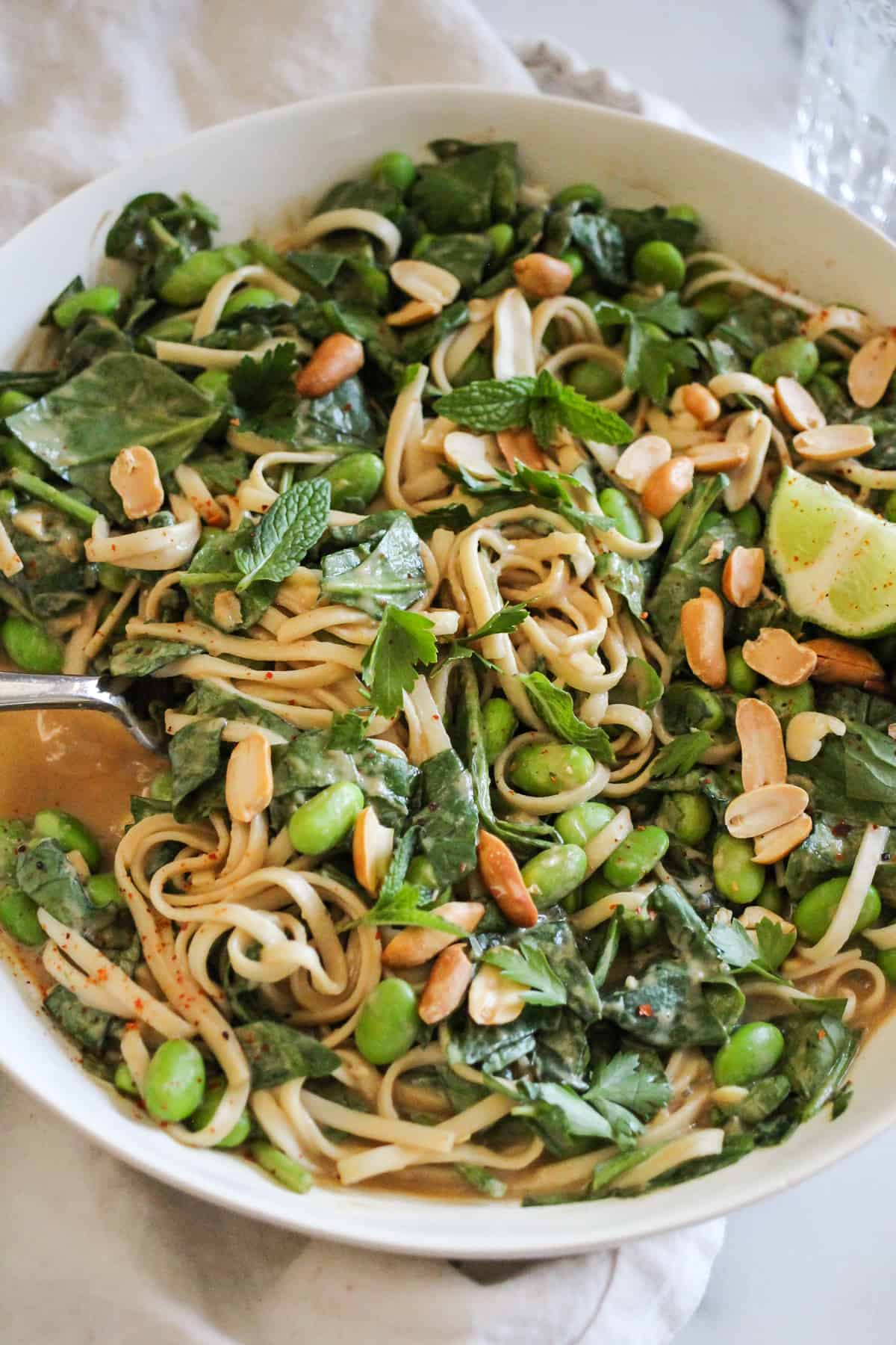 Peanut noodles with edamame and spinach in a white bowl.