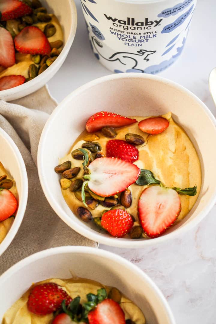 Four yellow turmeric yogurt bowls with nuts and fruit and a container of Wallaby Organic yogurt.