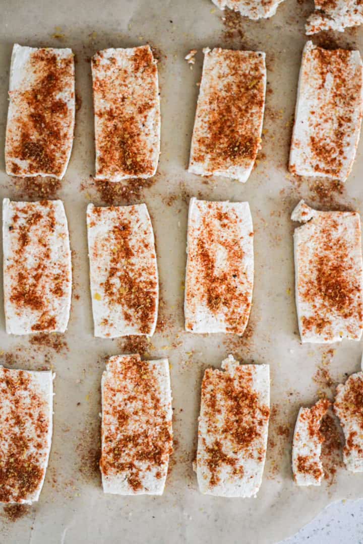 Tofu strips on parchment paper sprinkled with spices.