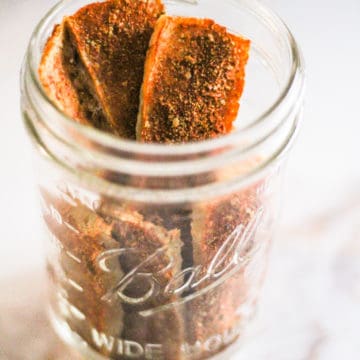 Tofu jerky in a glass jar on white counter.