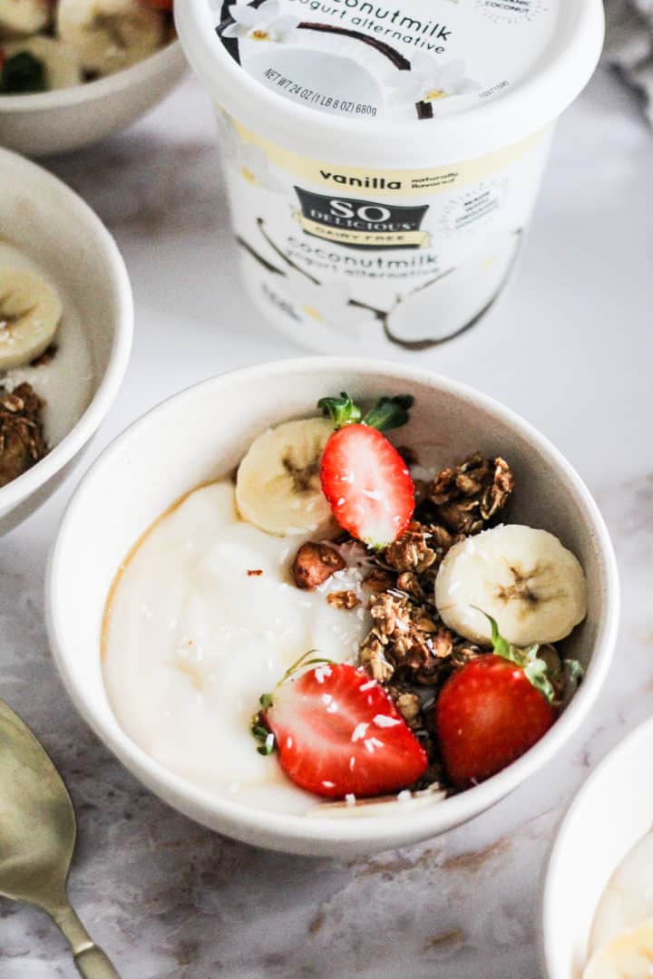 Closeup image of a vegan granola bowl with a container of So Delicious Yogurt Alternative behind it. 