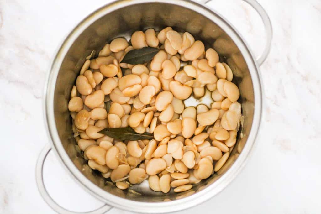 Horizontal image of butter beans and bay leaves cooking in a large pot.