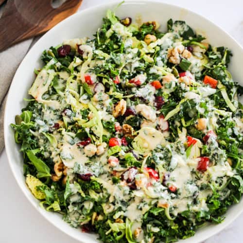 Meal prep salad with orange tahini dressing in a white bowl with wood serving spoons.