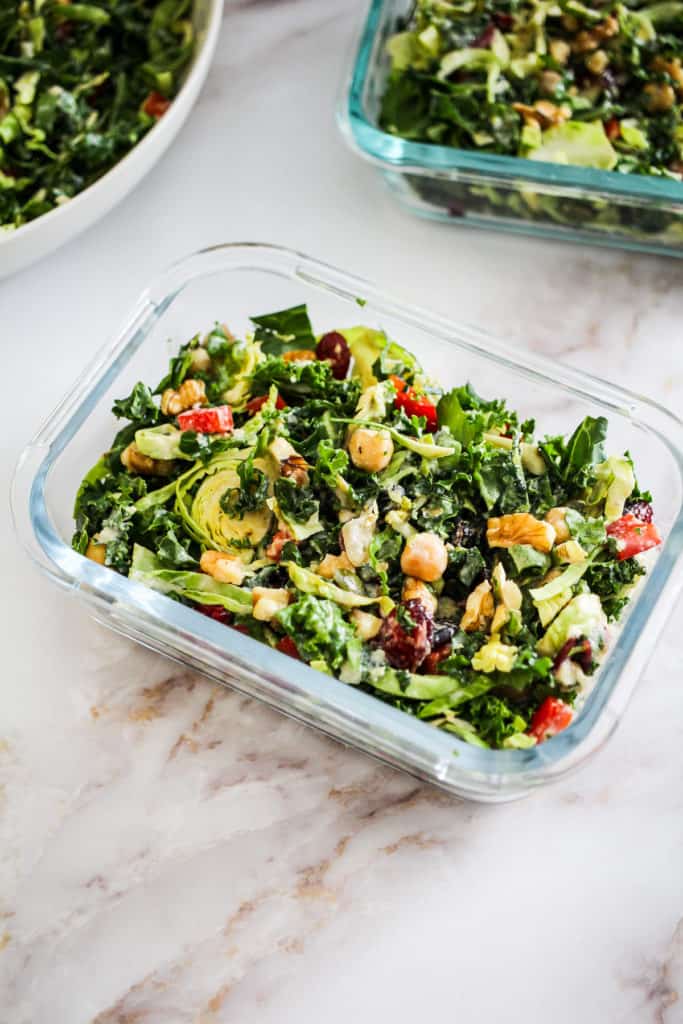Closeup image of meal prep salad in a glass container on white marble background.