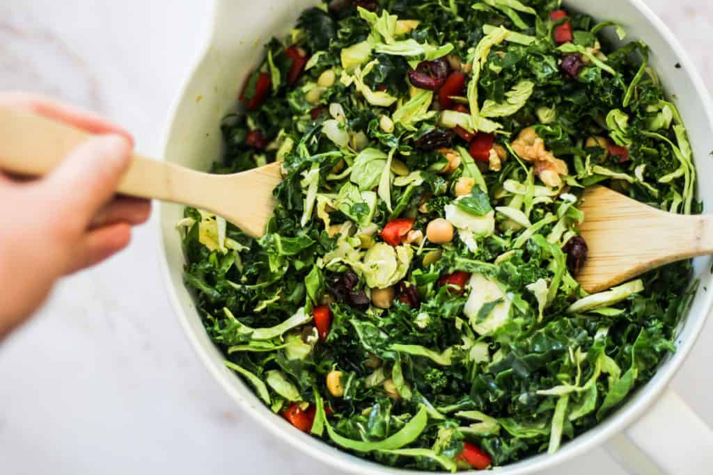 Horizontal image of mixing a green salad with wooden spoons.