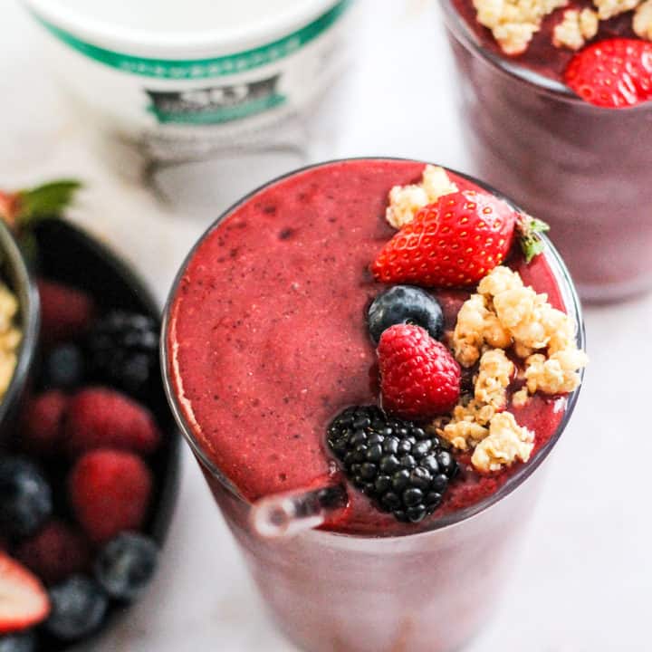 Berry Coconut Water Smoothie in a glass topped with fresh berries and granola with a tub of So Delicious yogurt alternative behind it.