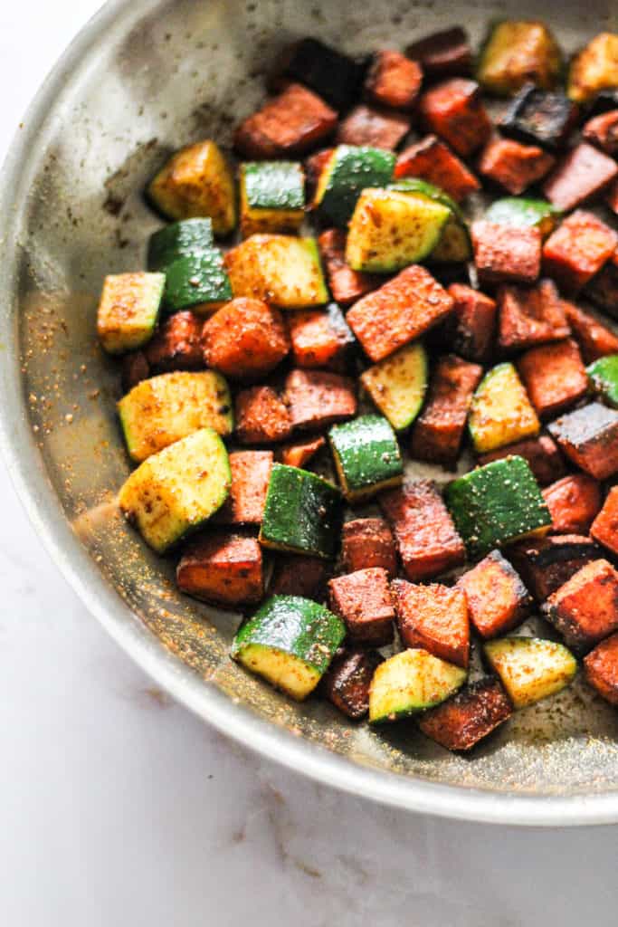Sautéed sweet potato and zucchini cubes in an all-clad skillet.