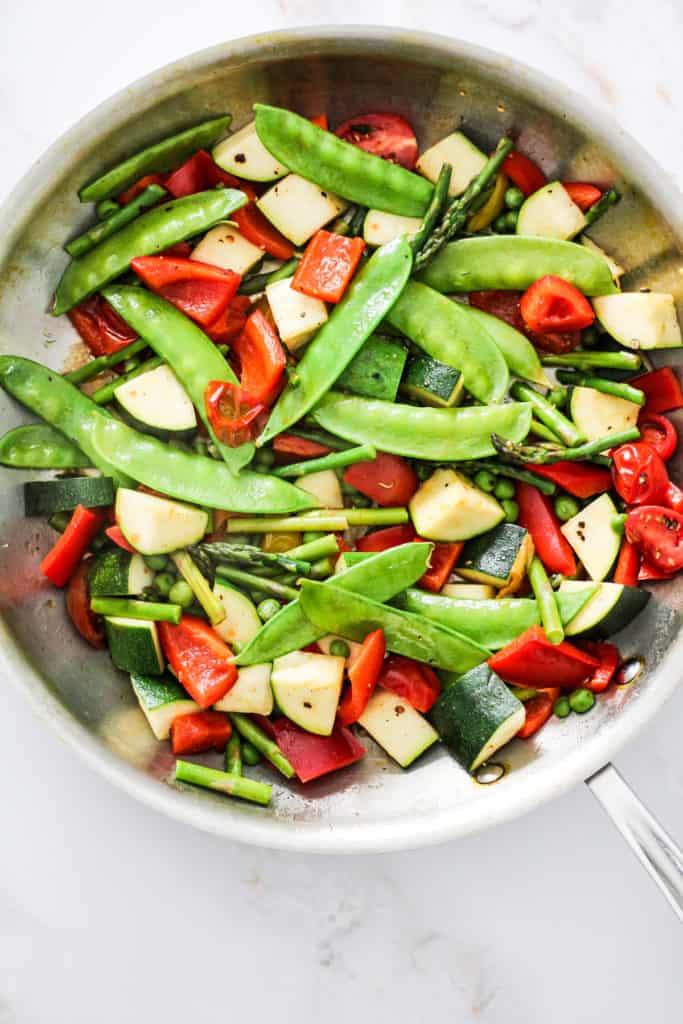 Sautéed snow peas, zucchini, red bell pepper, asparagus, and peas in a large skillet.