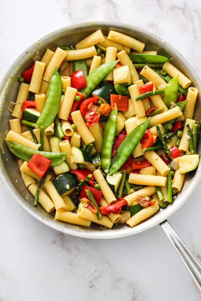 Vegetables and pasta in a skillet on a white marble countertop.