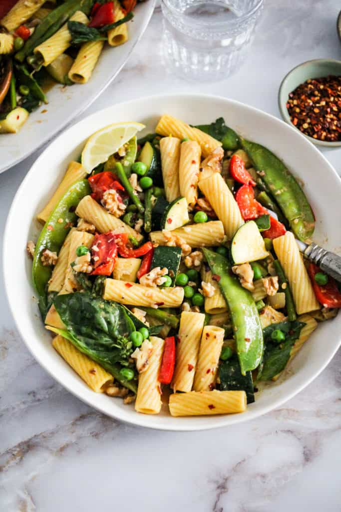 Vegetable rigatoni with walnuts in a white pasta bowl.