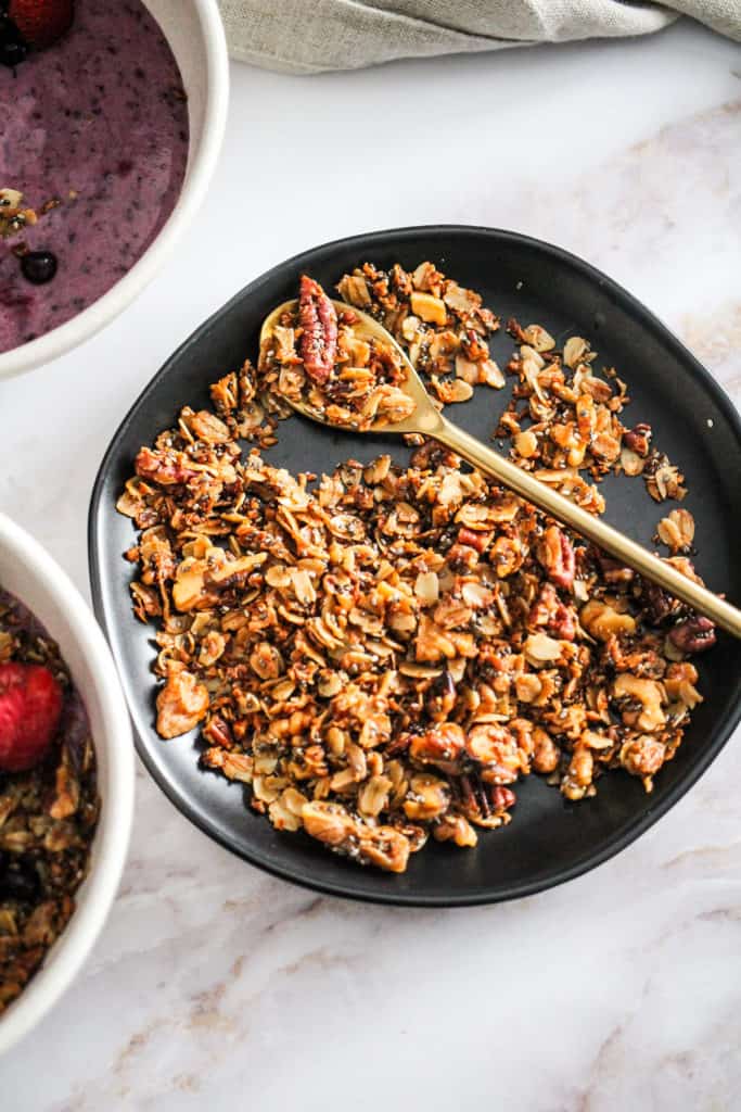 Homemade granola on a black plate with a gold spoon.