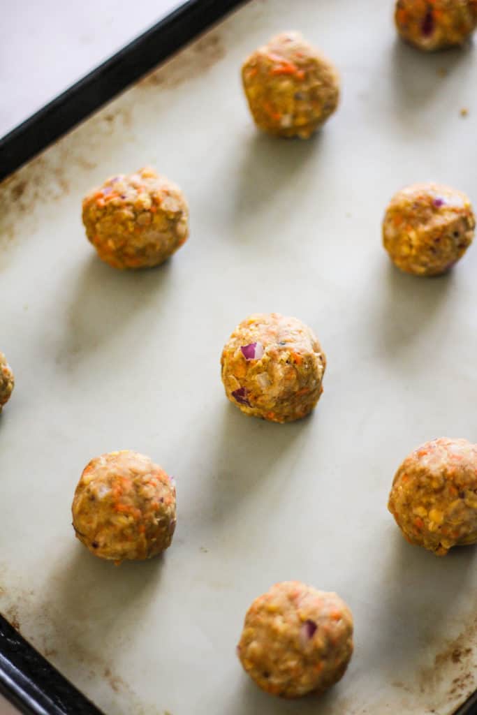 Uncooked falafel on a baking sheet lined with a silicone baking mat.
