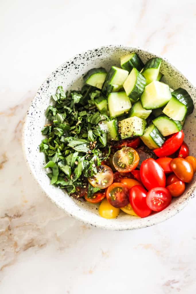 Bowl with cucumber, cherry tomatoes, and fresh herbs with salt and pepper.