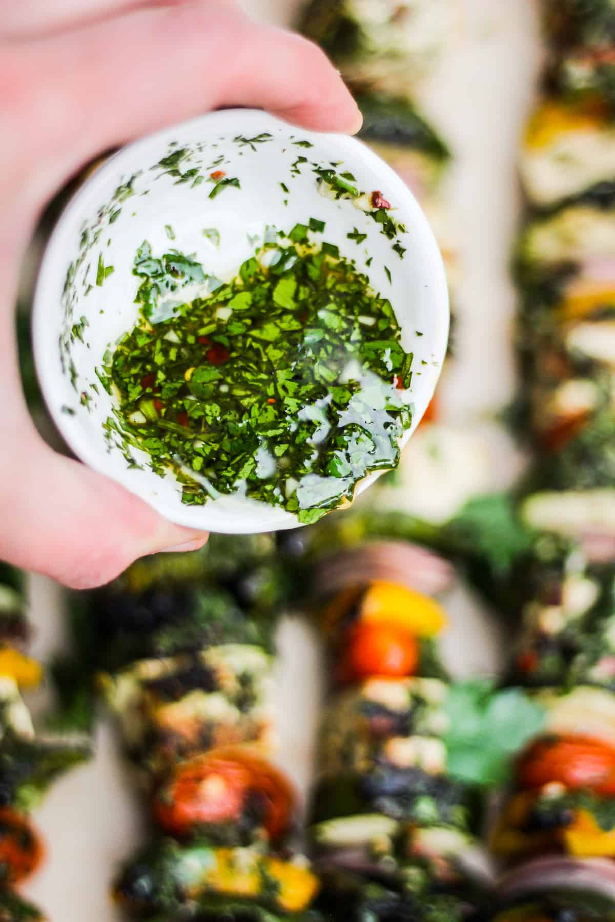 Closeup action shot of pouring chimichurri sauce on kebabs.